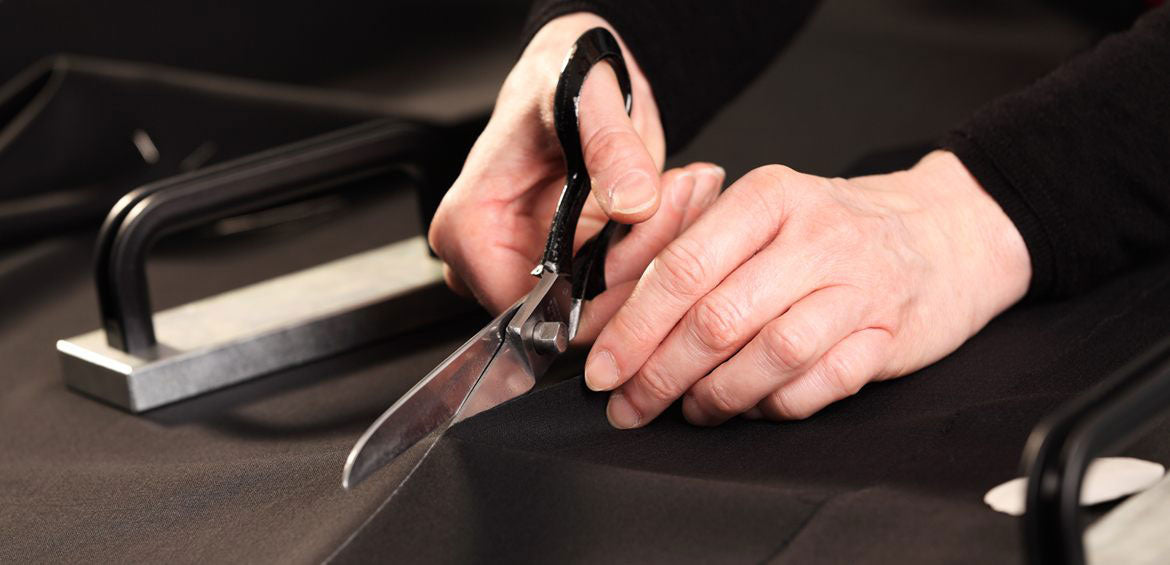 Hands cutting black fabric with tailoring shears