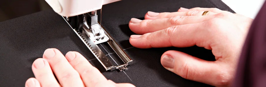 Sewing in the atelier: hands guide black robe cloth with chalk marks under the presser foot